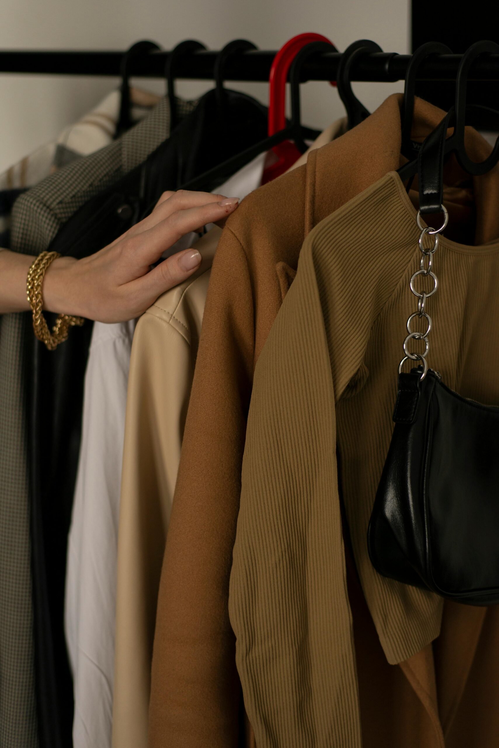 Hand selecting neutral-toned clothing on a modern fashion rack with accessories.